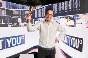 Marcel Esser mit einer Börsenglocke in der Hand vor einer LED-Wand beim ABOUT YOU Börsengang